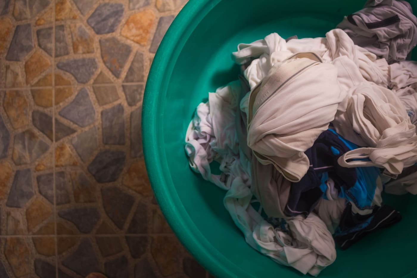 Green plastic basket of crumpled clothes seen from above on a tiled floor