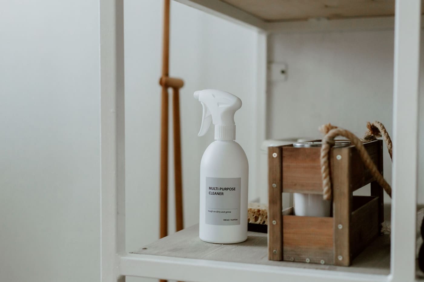 Spray bottle and a small wooden caddy of cleaning supplies on a white shelf