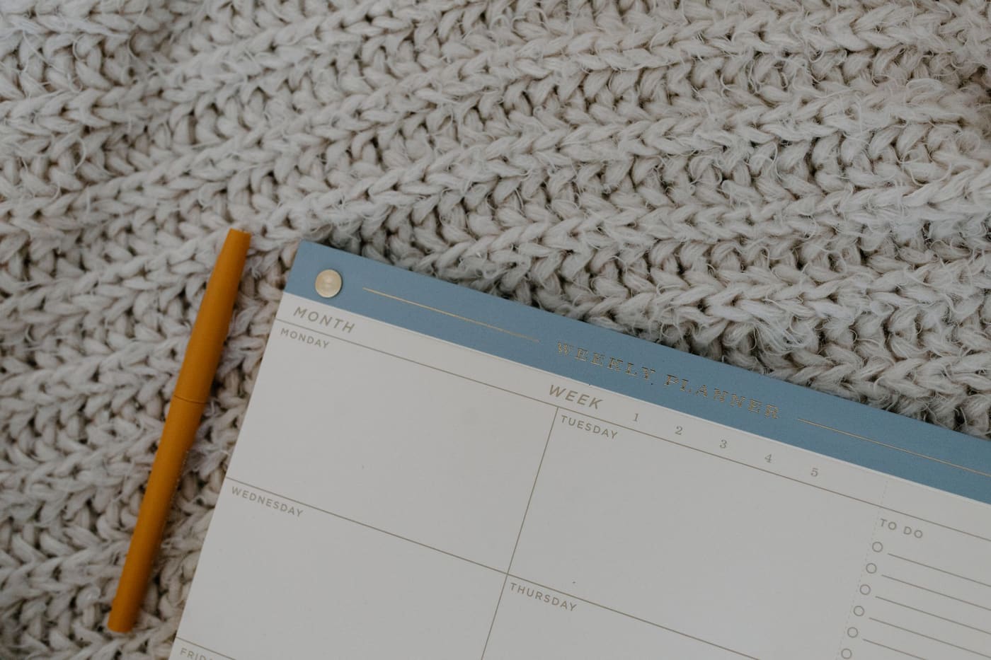 Weekly planner pad and a mustard-yellow pen on a chunky knit blanket